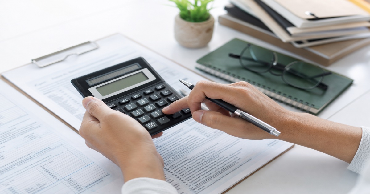 Hands using a calculator beside tax worksheets during self-employment tax calculation